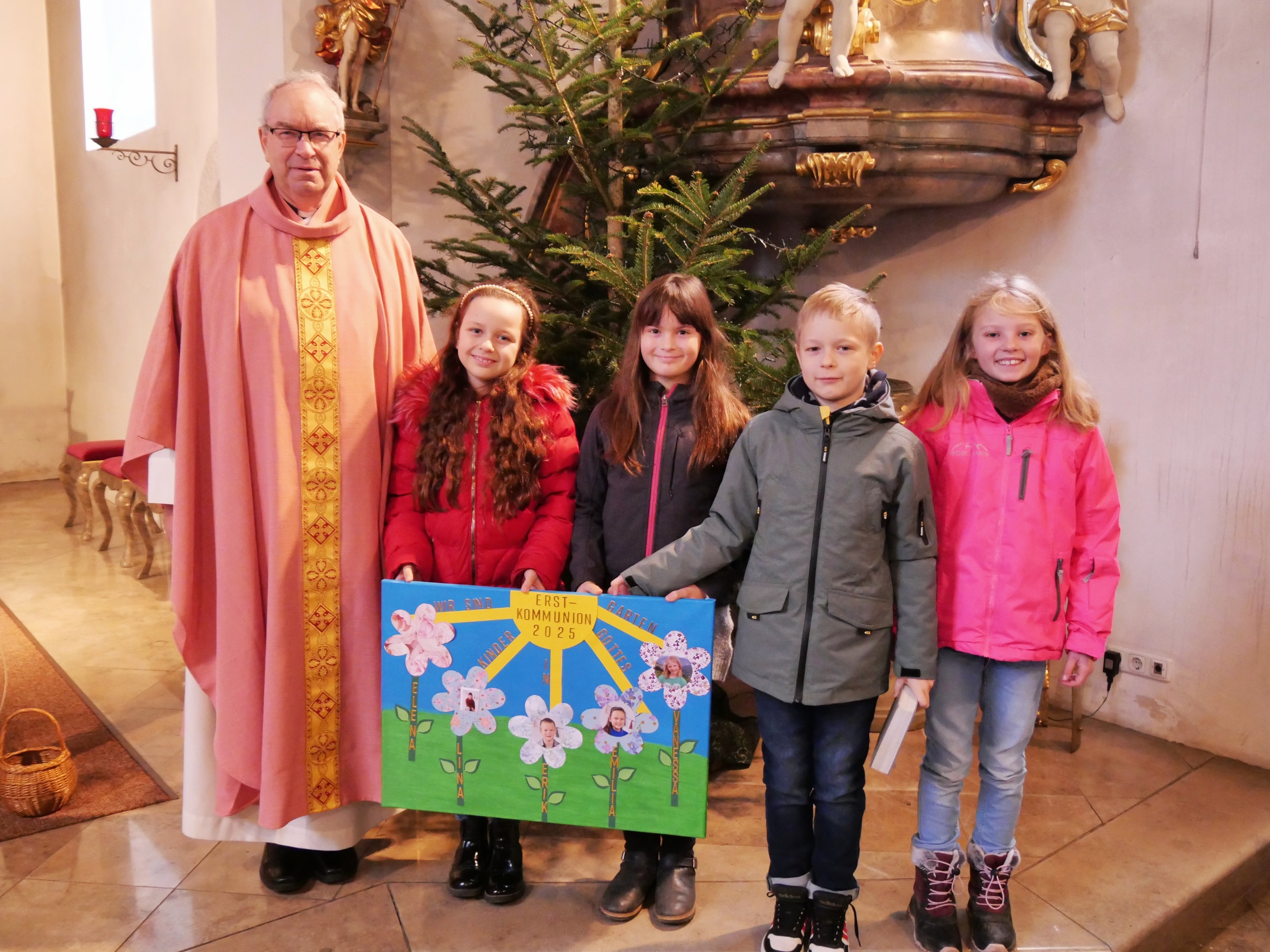 Gruppenbild mit Pfarrer Rügamer, vier Kommunionkindern und dem Vorstellungsplakat.