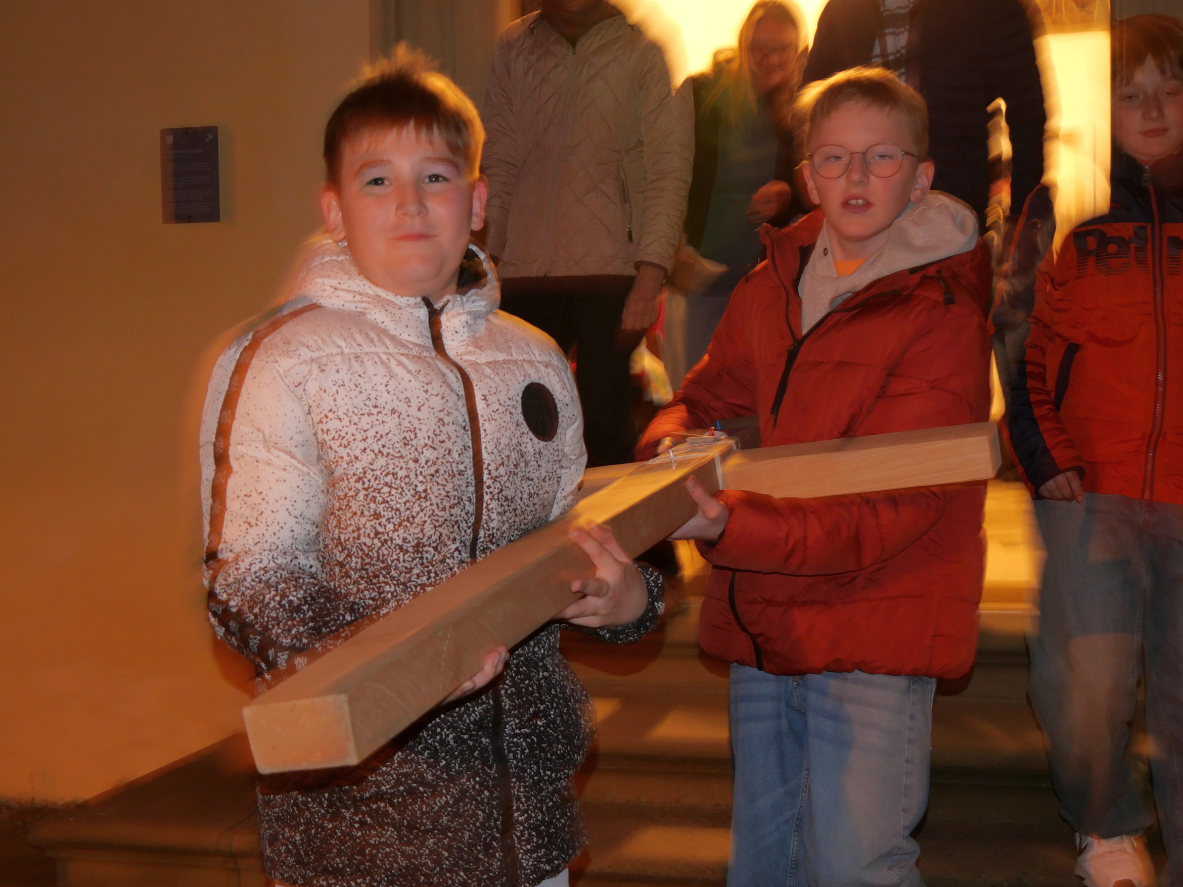 Zwei Kinder tragen ein Holzkreuz mit ihren Händen.