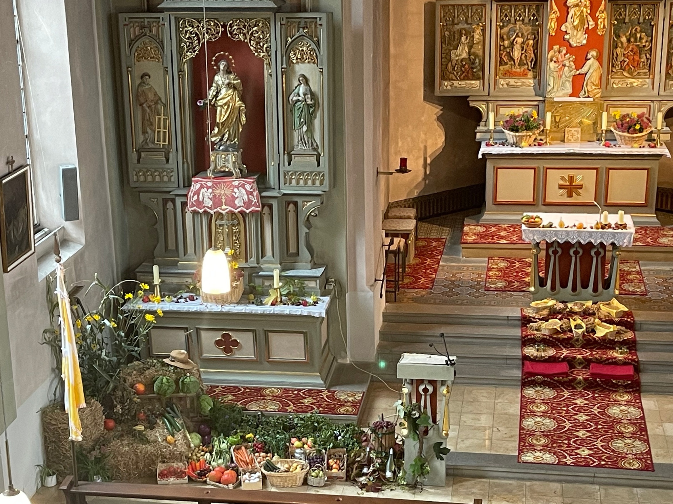 Das ist ein Foto von der Empore herunter in die Kirche. Man sieht den Seiten- und Hauptaltar. Dort ist es herbstlich dekoriert.
