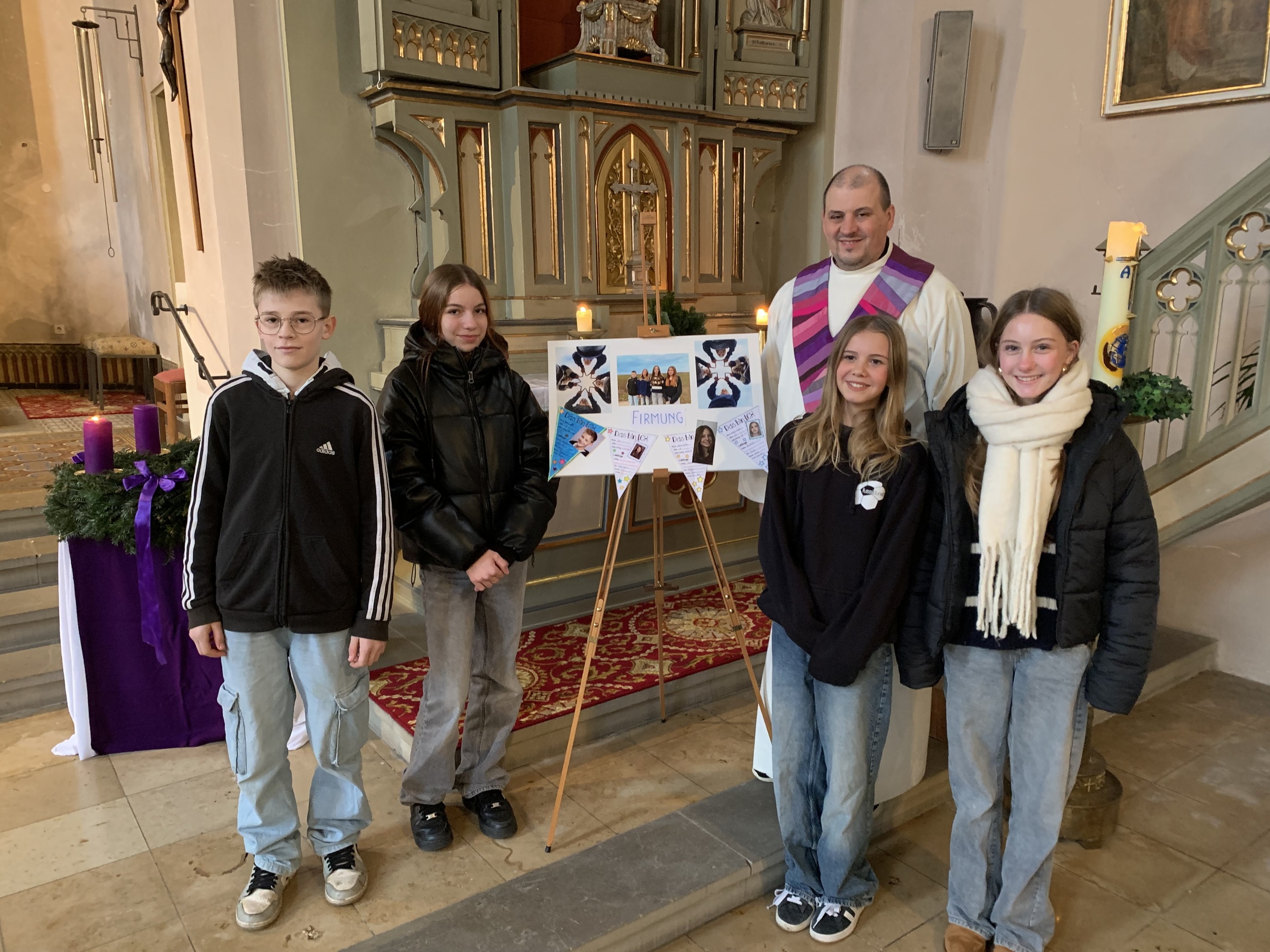 Die vier Firmlinge aus Opferbaum und der Pastoralreferent stehen auf den Altarstufen in der Kirche und zeigen ihr Plakat.