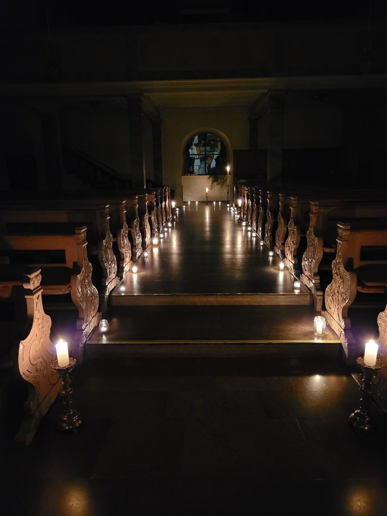 Blick von vorne nach hinten, den Mittelgang entlang stehen viele Kerzen und beleuchten so die Kirche