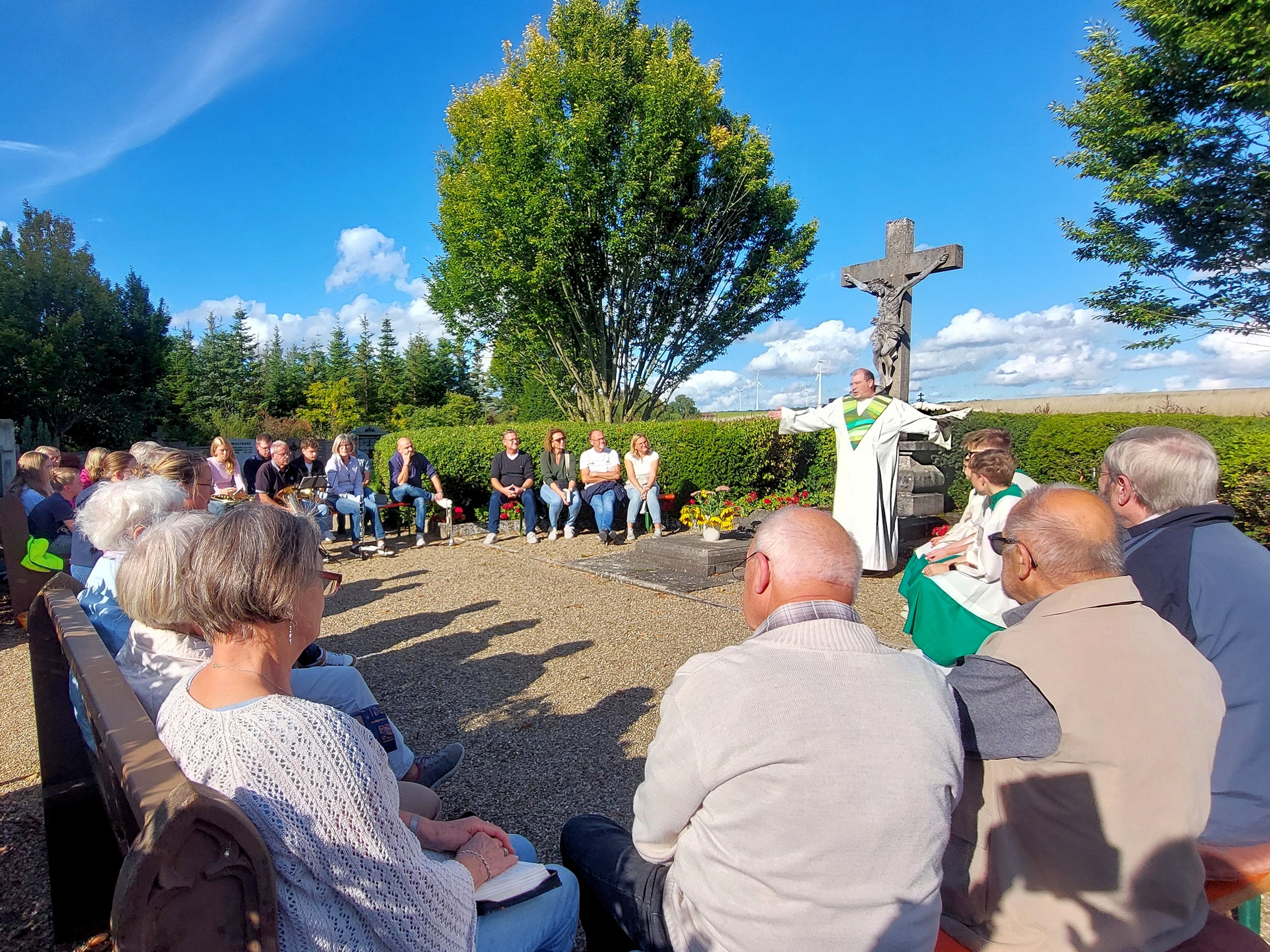 In einem Kreis sitzen Menschen um das Kreuz im Friedhof.