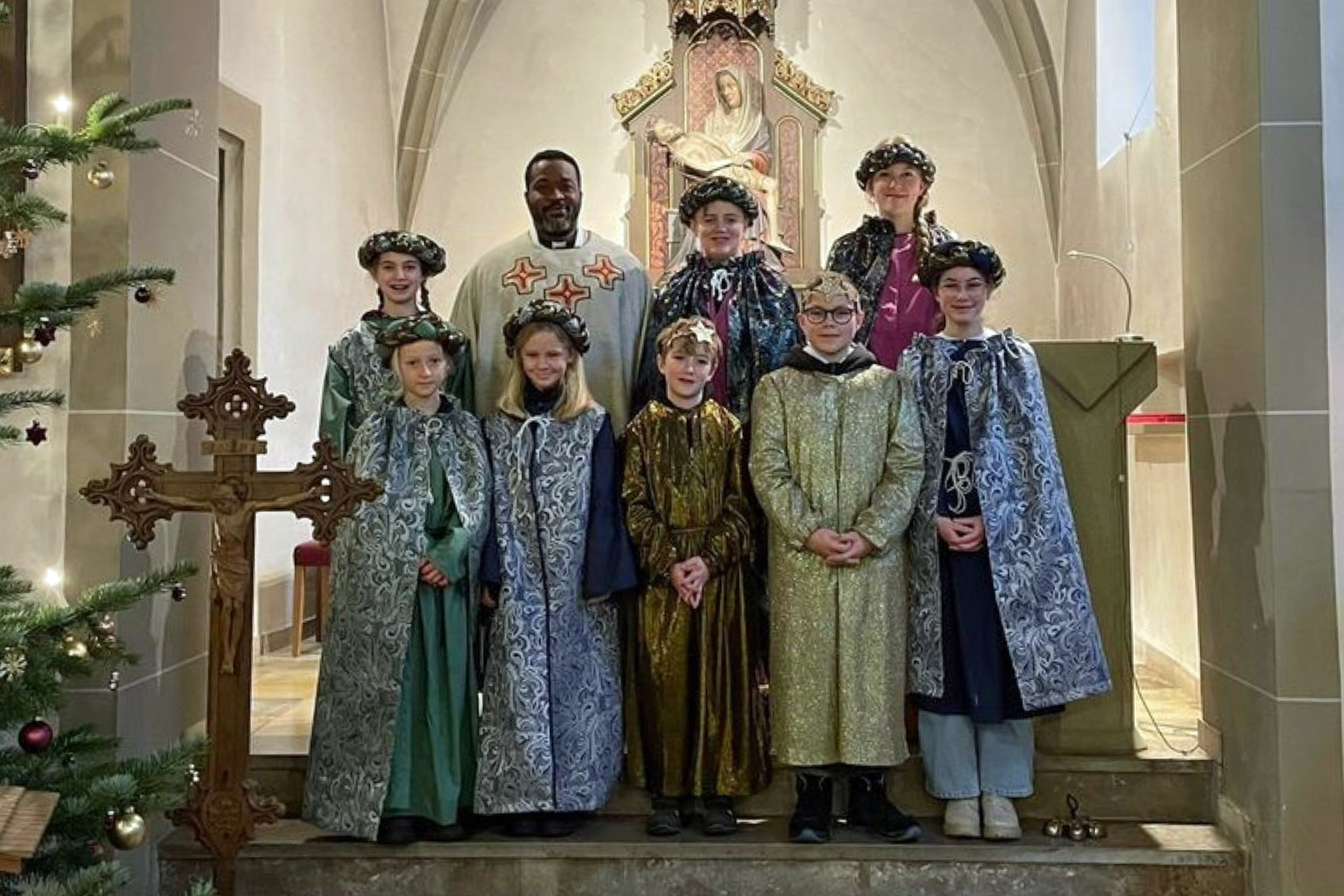 Ein Gruppenbild der Sternsinger im Altarraum der Kirche mit Kaplan Louis Odidi