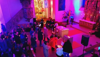 Blick von der Empore in den Kirchenraum. Die Besucher halten ein brennendes Teelicht in der Hand und bringen es nach vorne, um es beim Evangelium abzustellen. Dabei spielt die Band im Hintergrund Musik.