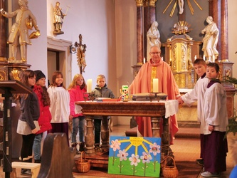 Pfarrer Rügamer und die Kinder stehen um den Altar und fassen sich an den Händen
