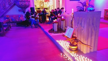 etwa 100 Teelichter stehen vor dem Ambo auf dem Boden, im Hintergrund sieht man die Band und den brennenden Adventskranz