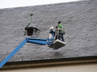 In der Höhe des Schieferdachs der Wallfahrtskirche arbeiten zwei Männer.