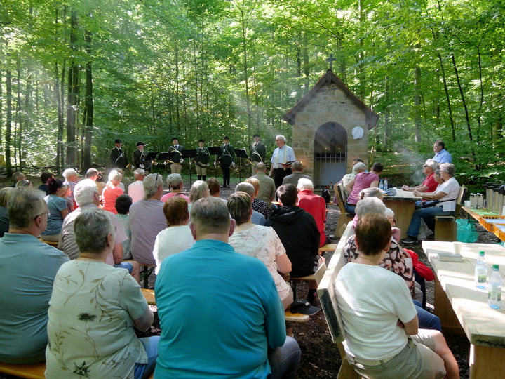 Eine Gesamtübersicht von hinten über Menschen hinweg zur Waldkapelle hin.