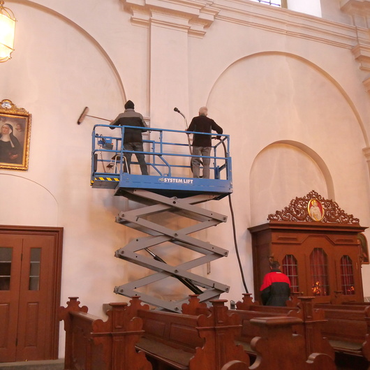 Zwei Männer reinigen mit dem Staubsauger und Besen eine Kirchenwand.