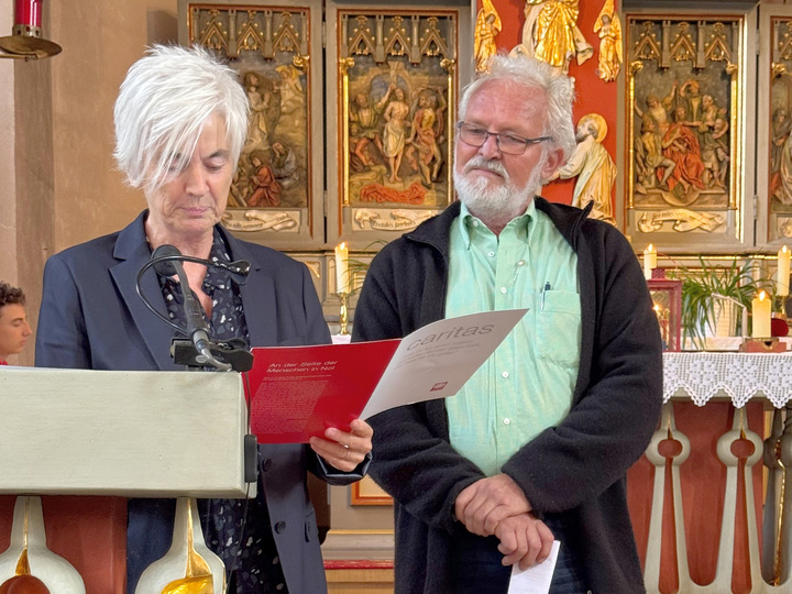 Am Ambo stehen die zwei Personen. Frau Eitzenberger hat die Urkunde in der Hand und liest sie vor.